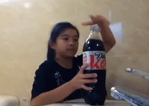 A little girl opens a 2L bottle of Diet Coke which proceeds to spill all over the place. The girl has a look of pure terror on her face as she panics to extinguish the liquid.