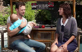 Joel Mchale grabs a little boy by the leg and hands it to a lady while the child is upside down.