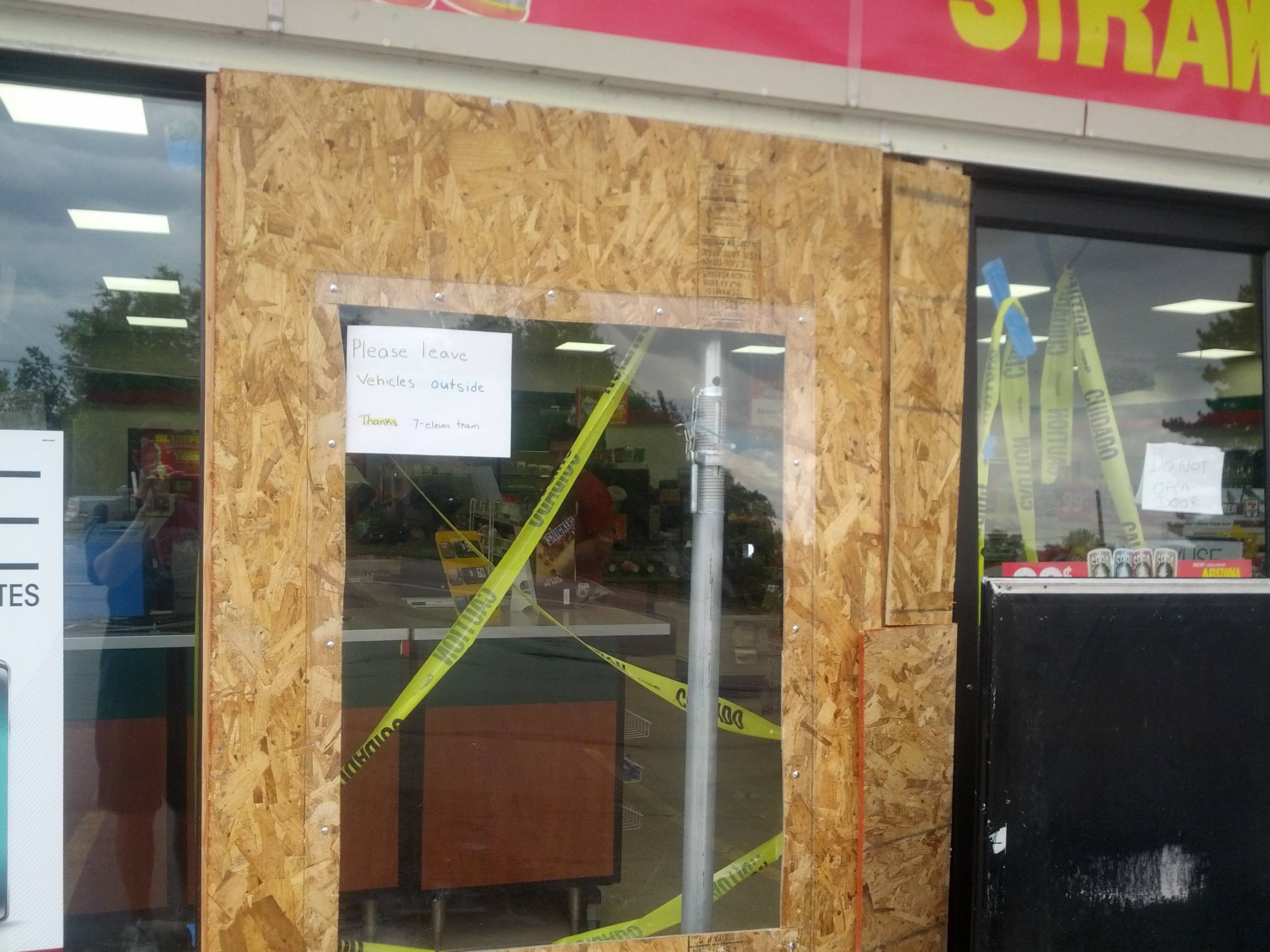 The door of 7/11 has been replaced by plaster and is being repaired because a car drove through it. A paper says please leave cars outside.