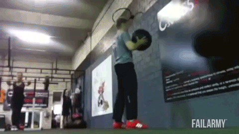 A guy with a weighted ball throws it in the air squats down and does a push up before getting knocked out by the ball.